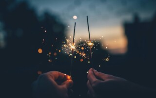 Two hands holding sparklers at dusk